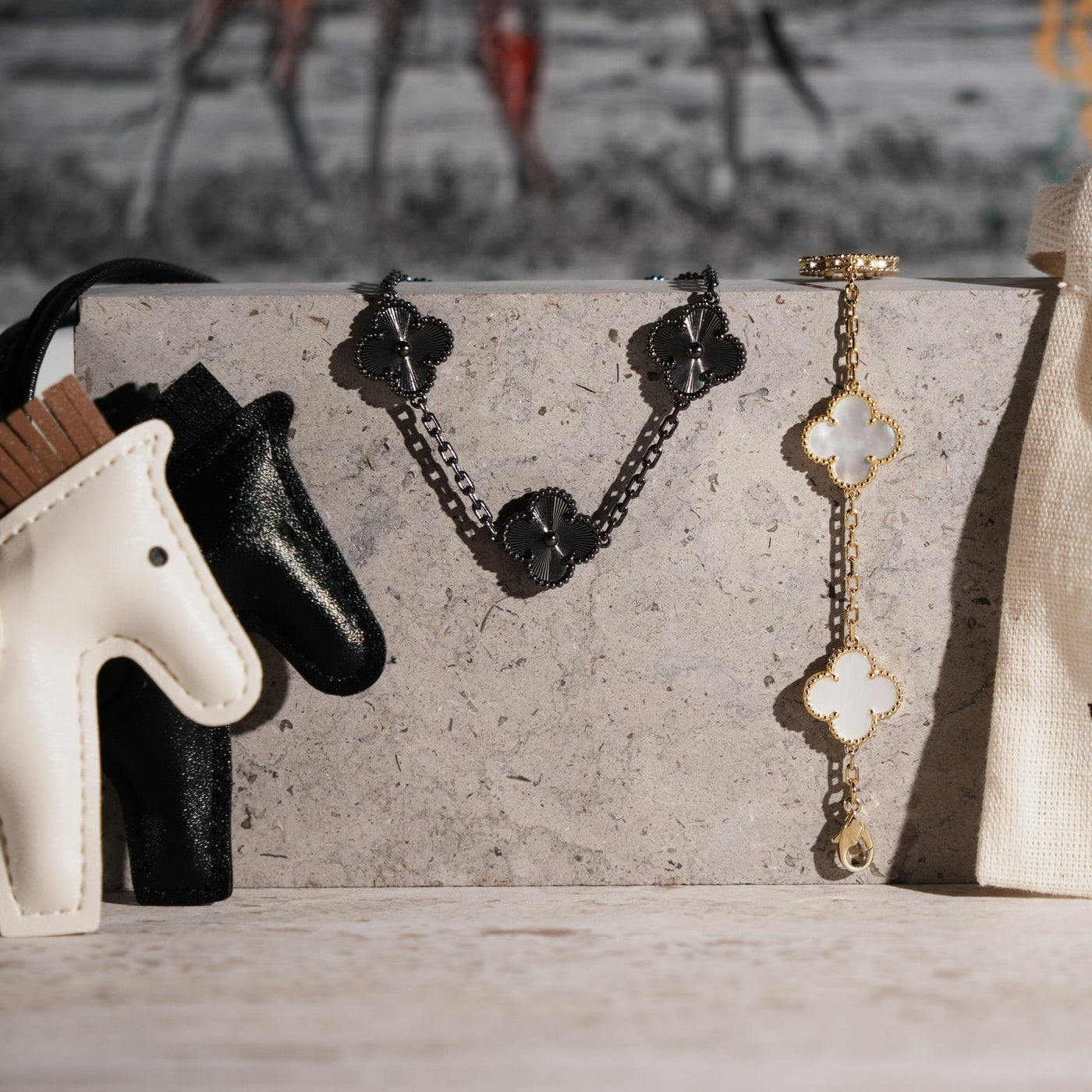 Fleuron Paris Clover Bracelet in black tungsten carbide displayed on a stone surface beside a gold clover bracelet, showcasing its unisex, elegant style.