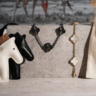 Fleuron Paris Clover Bracelet in black tungsten carbide displayed on a stone surface beside a gold clover bracelet, showcasing its unisex, elegant style.