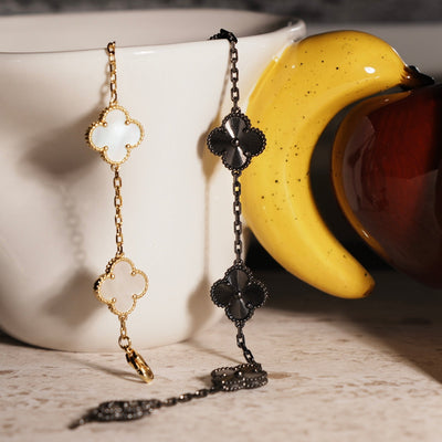 Black tungsten carbide Fleuron Paris Clover Bracelet hanging beside a gold clover bracelet, highlighting the contrast in finishes and luxury appeal.